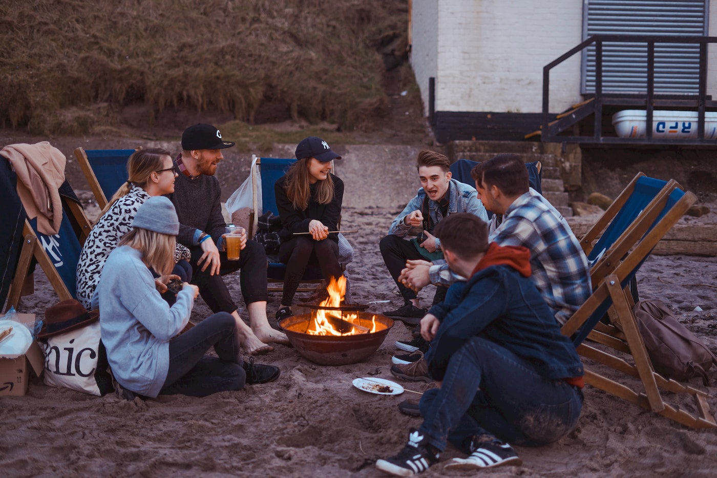 Group of friends drinking beer and hanging out around a fire on the beach.