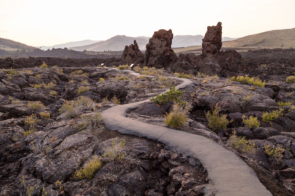 a paved trail winds around lava rocks in craters of the moon, idaho