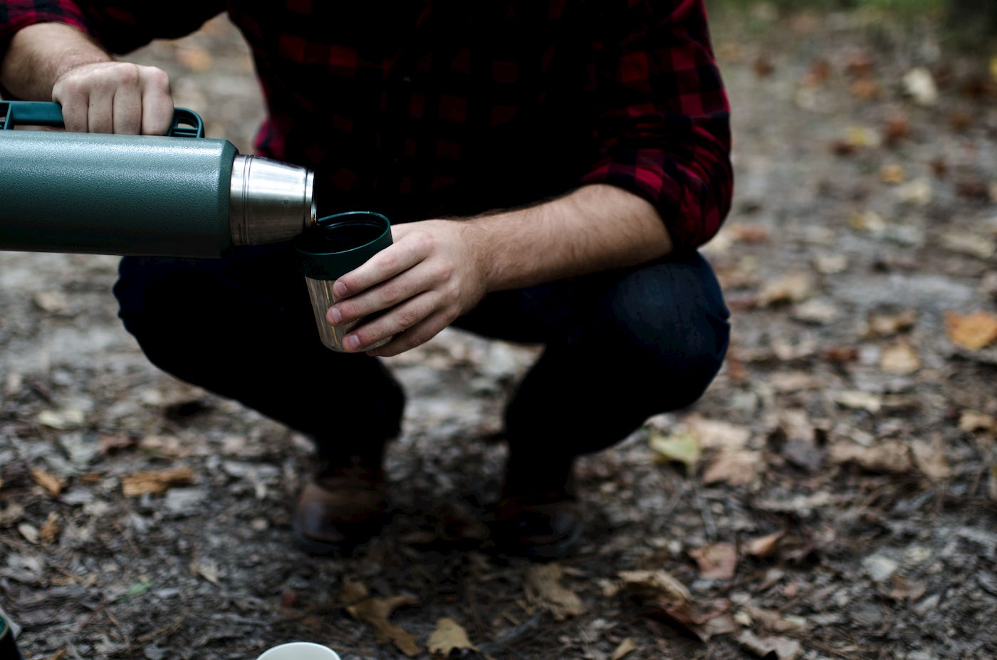 Person pouring coffee from a thermos outdoors.