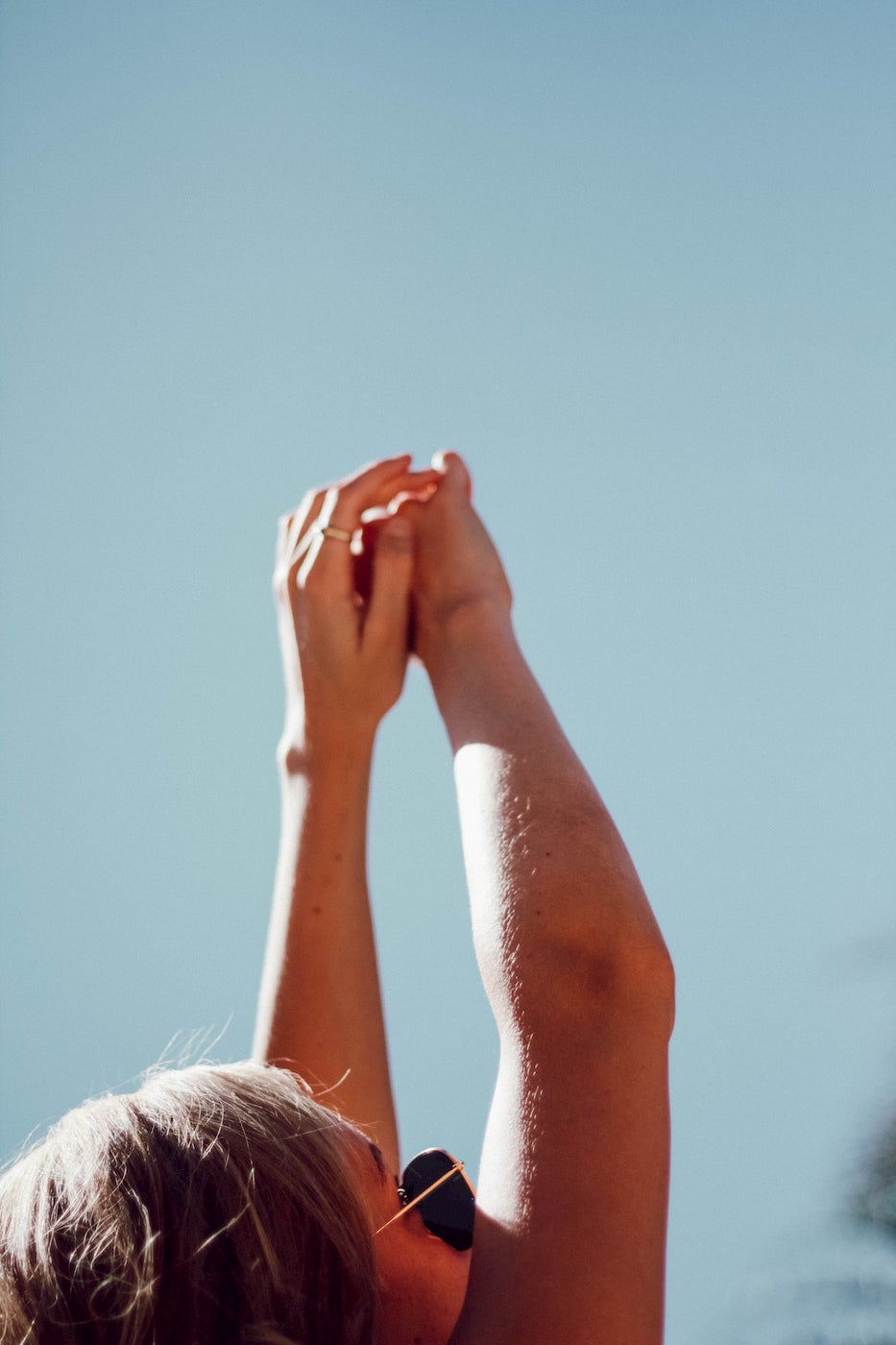 Women stretching her hands up towards the sky on a sunny day.