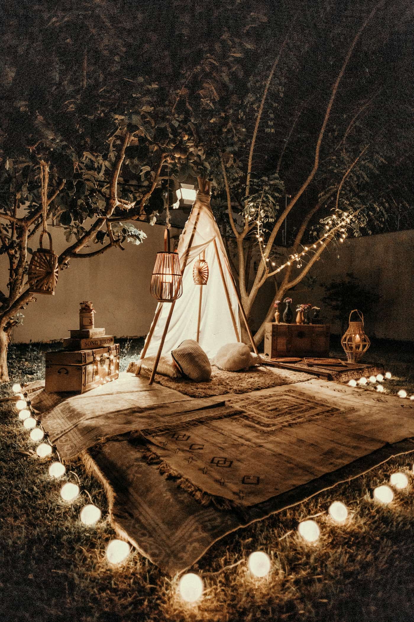 Glamping site setup in a backyard with lanterns and rugs.