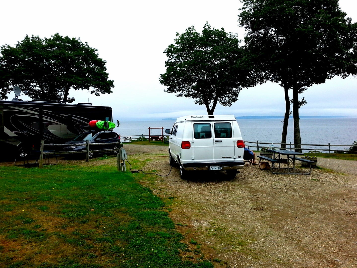 Van parked in campsite beside picnic table, trees, and the ocean.