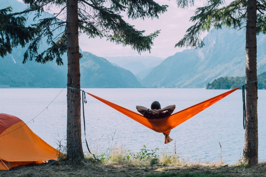 a man sitting in a hammock near a lake next to a tent