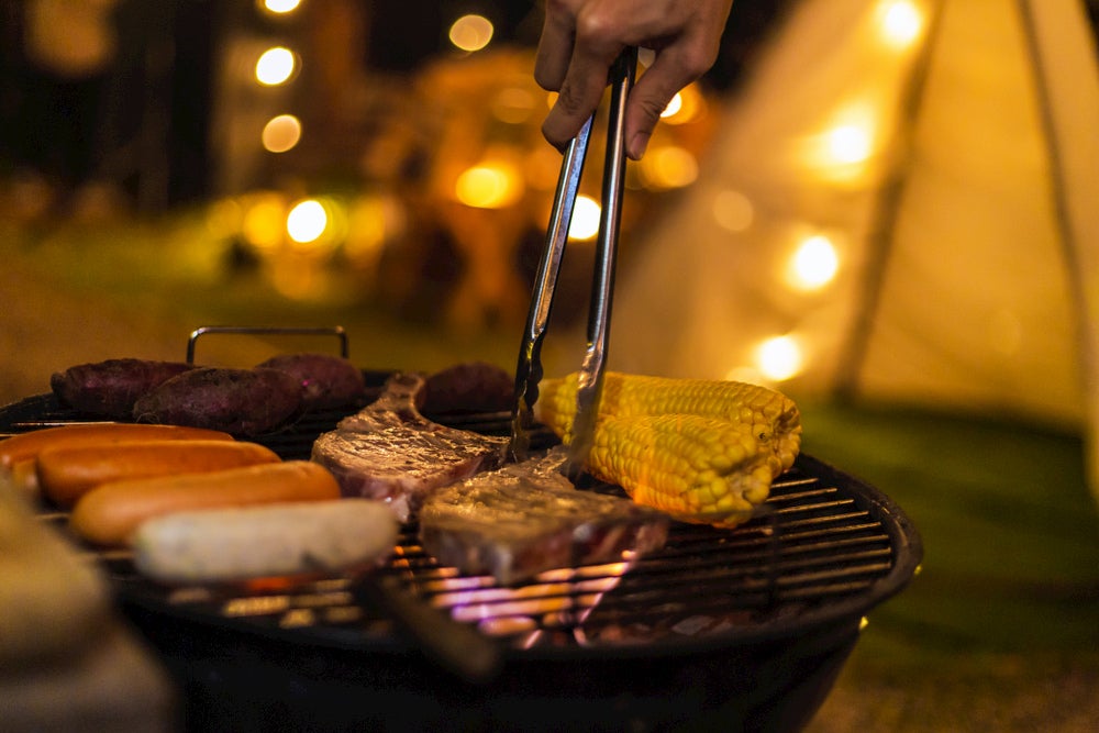 Grilling meet on and corn on a charcoal grill.