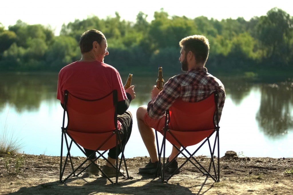 two men sitting in camping folding chairs by a river