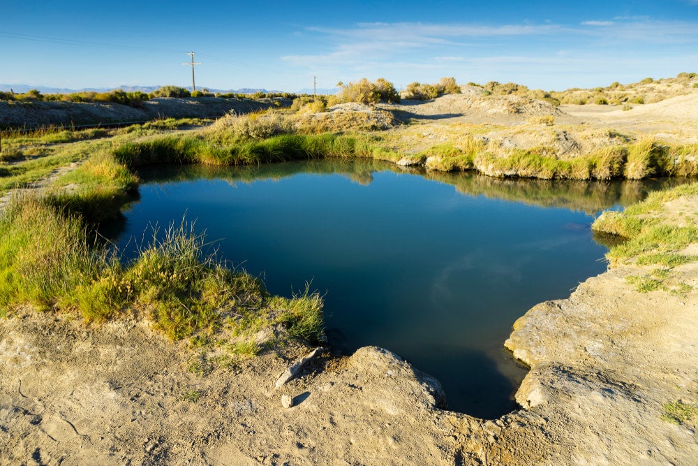a wide angle shot of a blue hot spring in the desert of nevada