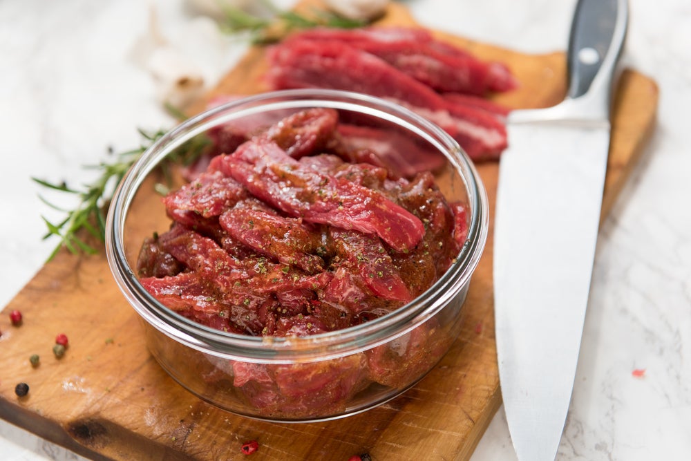 Meat with marinade in glass bowl on wood 