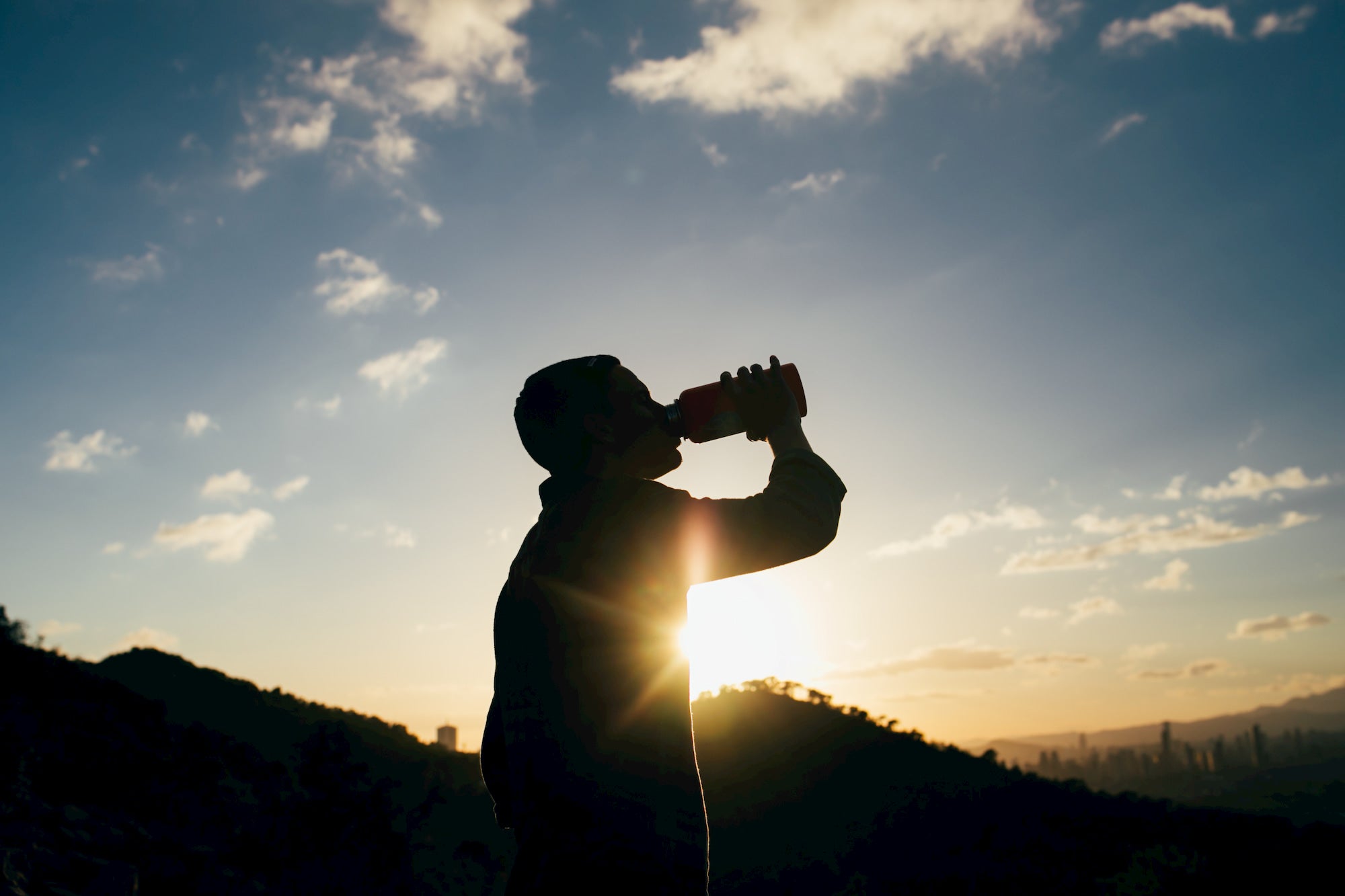 Silhouette of person drinking water during sunrise.