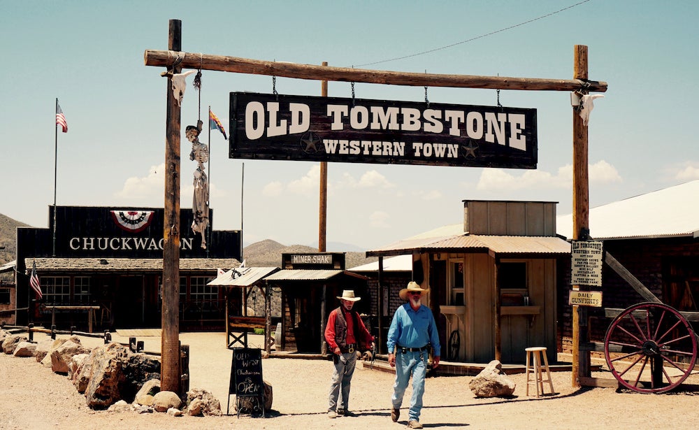 Twee mannen lopen onder Old Tombstone-bord in Arizona