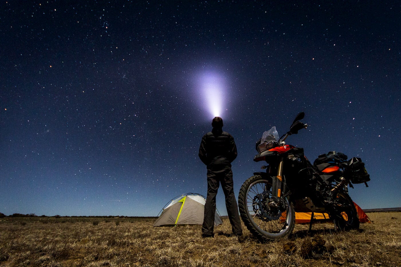 Motorcycle camper standing beside his tent in an open field.