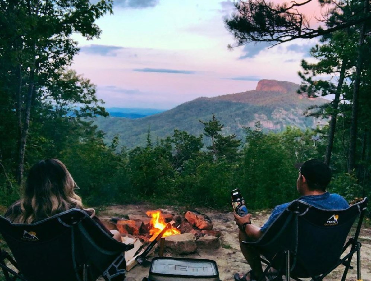 Two people sitting in GCI cahirs in the woods overlooking a sunset.