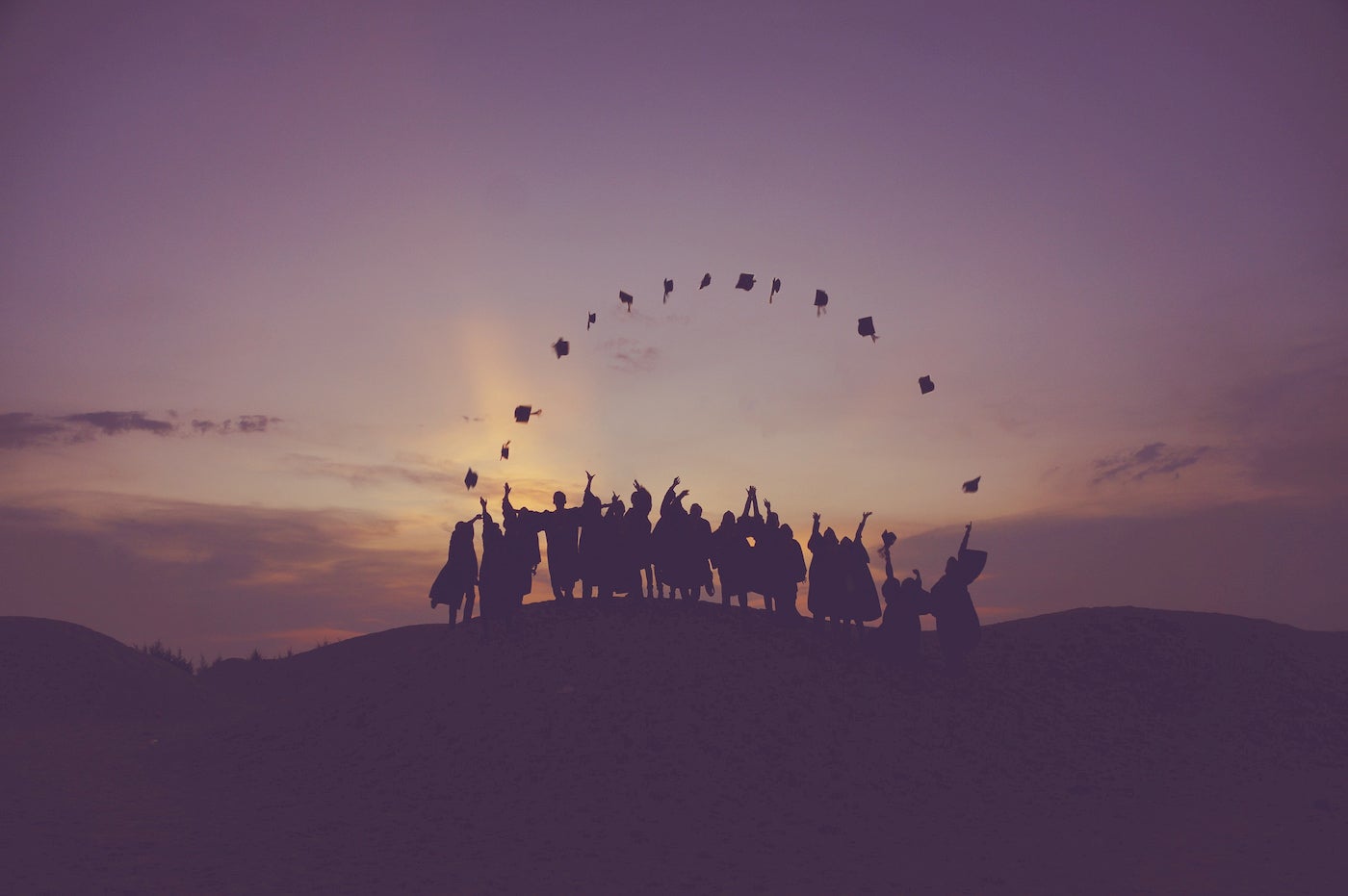 Silhouttes of graduates throwing their caps on a mountain.