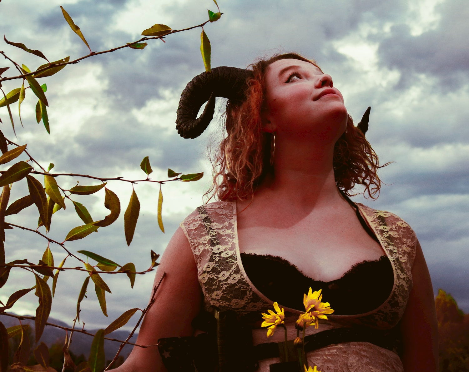 Female wearing horns and a lace dress in the forest.