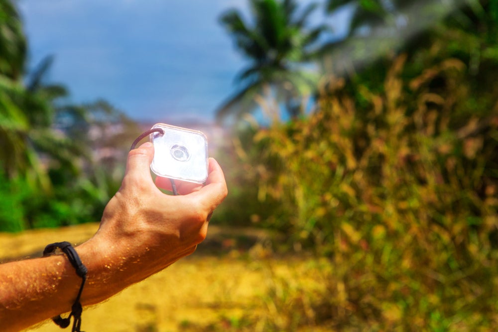 an outdoors signal mirror held by a man's hand during the day in the tropics