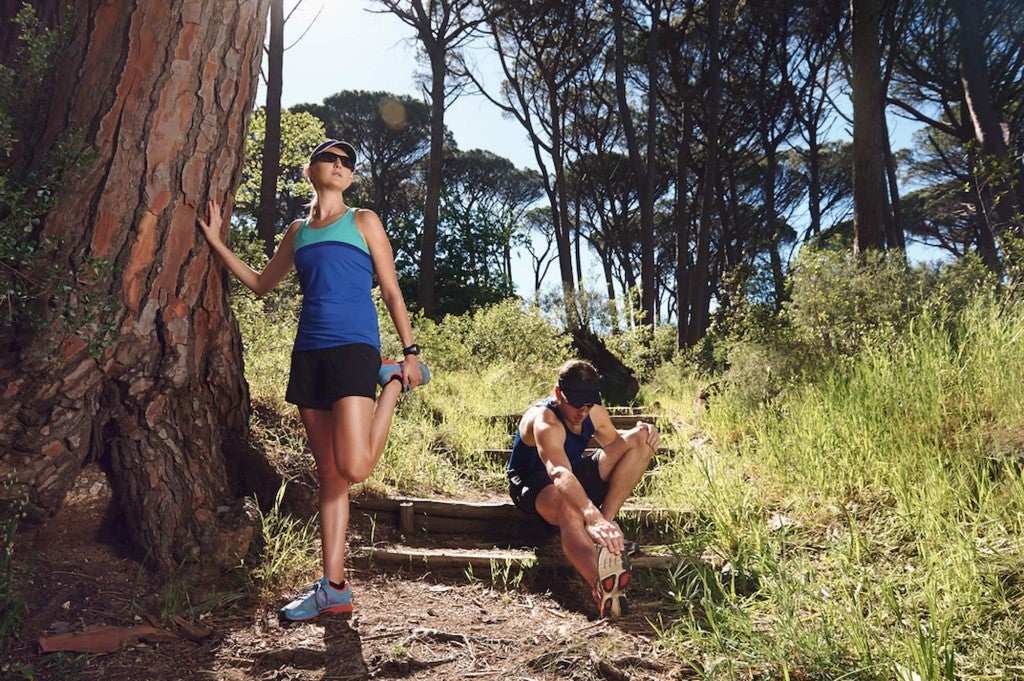 Trail runners stretching on forested trail.