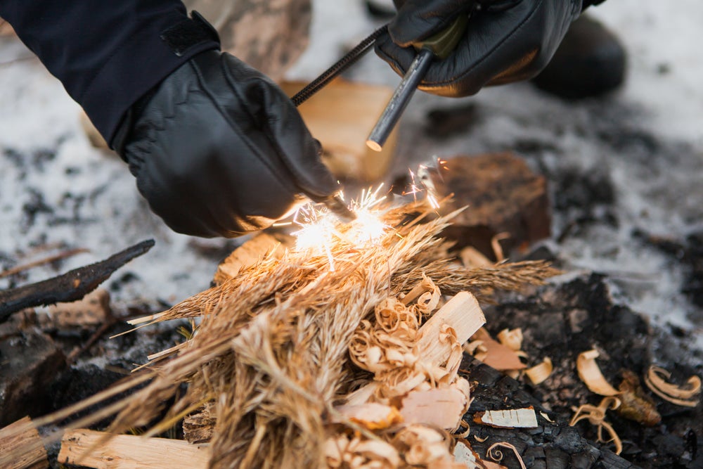  man holds a firestarter near a bundle of tinder and strikes