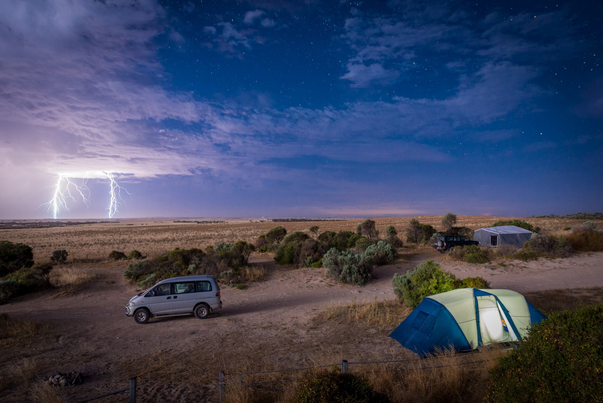 Lightning stirking in a prairie witha tent and van in the foreground.