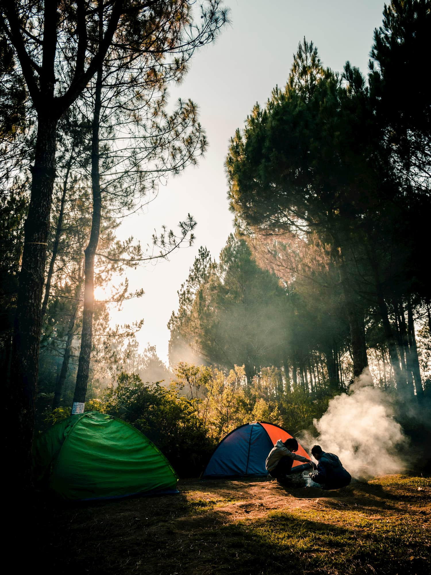 Campsite in the woods with two tents and a two people starting a fire.