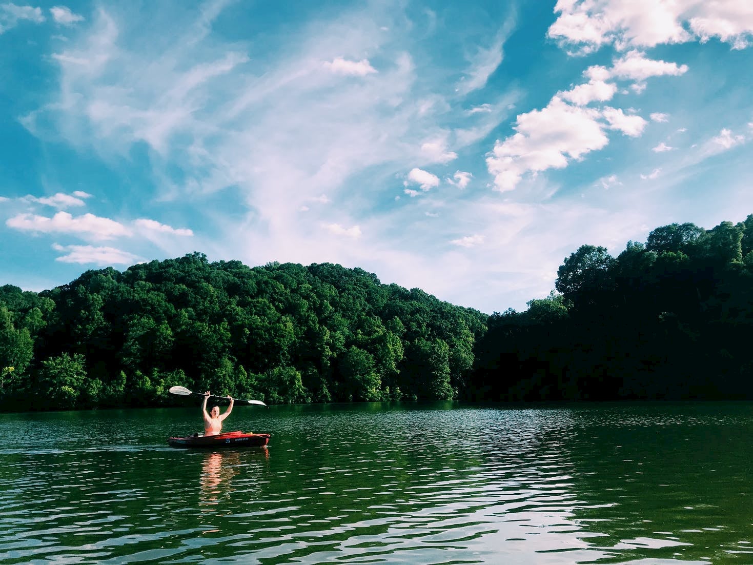 Kayaker raising their paddle overhead while floating in a lake.