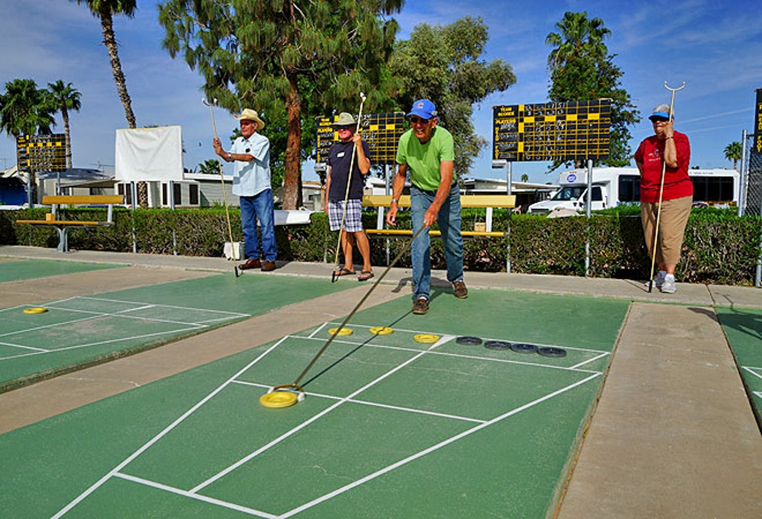 Elderly retirees playing shuffleboard outdoors surrounded by palm trees.