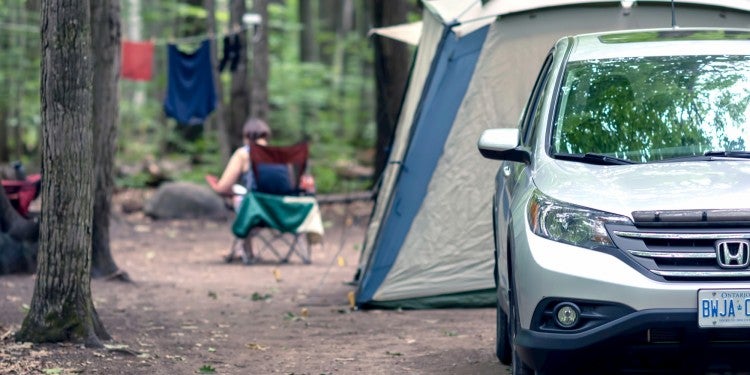 Car parked in front of campsite with tent and clothesline.