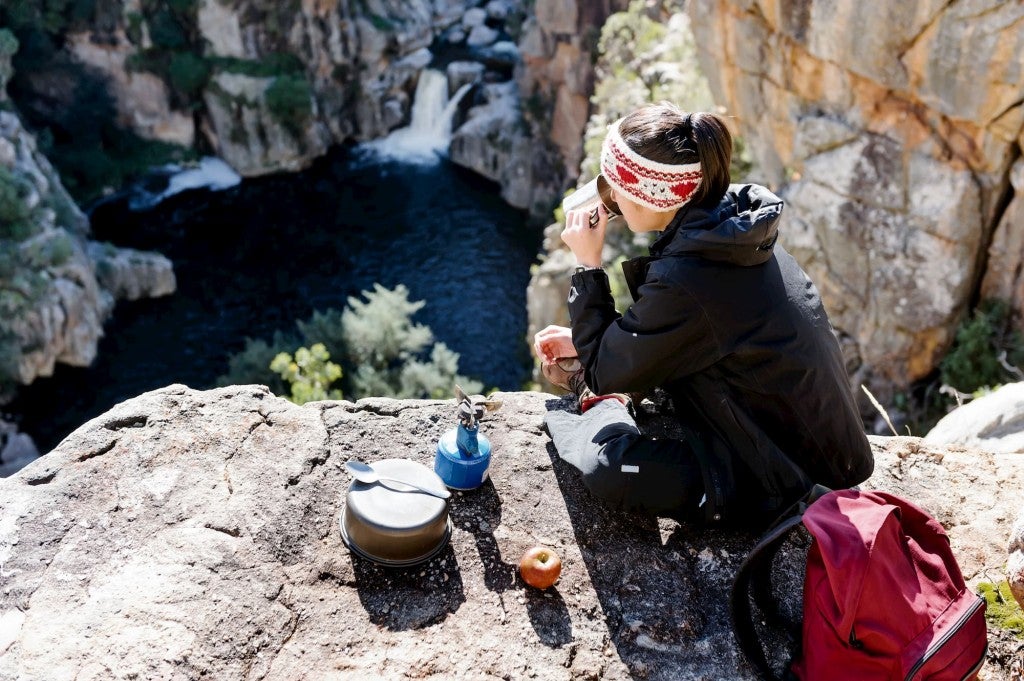 Backpacker cooking on a stove over scenic overlook.