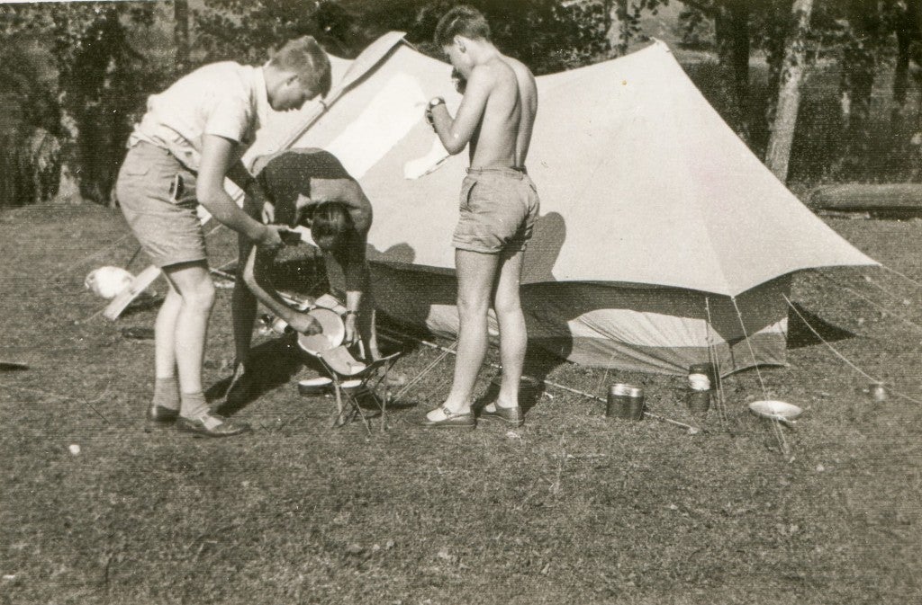 3 young men setting up a stove at a campsite.