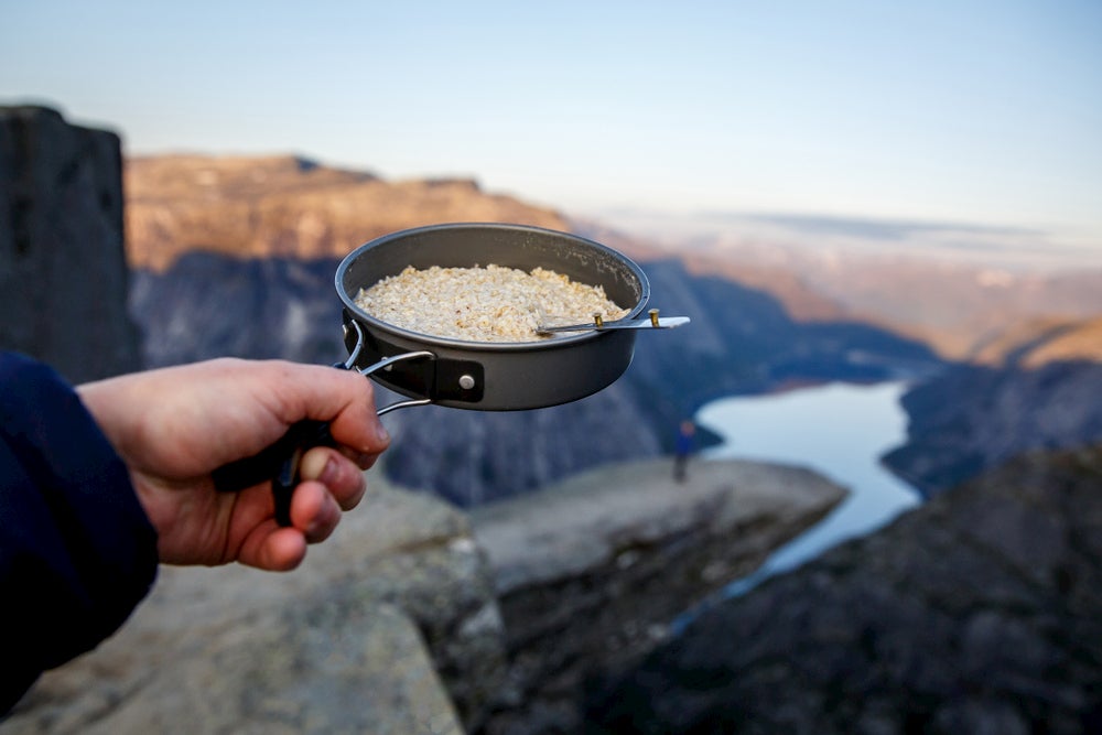 Camper eating oatmeal out of a backpacking pot at a scenic overlook.