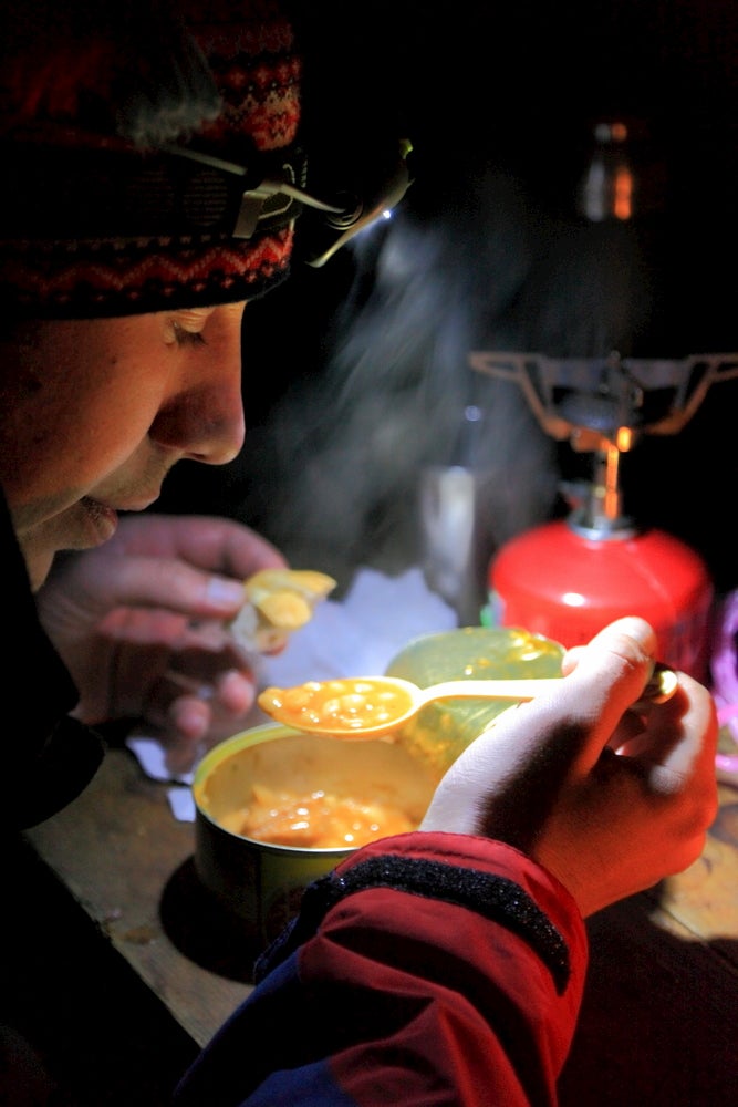 Backpacker eating soup under the light of their headlamp.