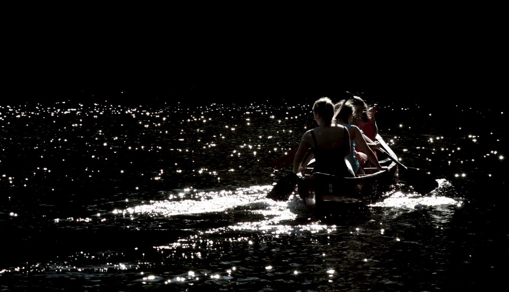 Group of women paddling a canoe under the moonlight.