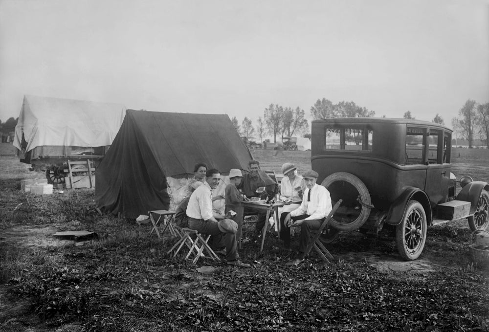 Group of people eating at a table at a car campsite.