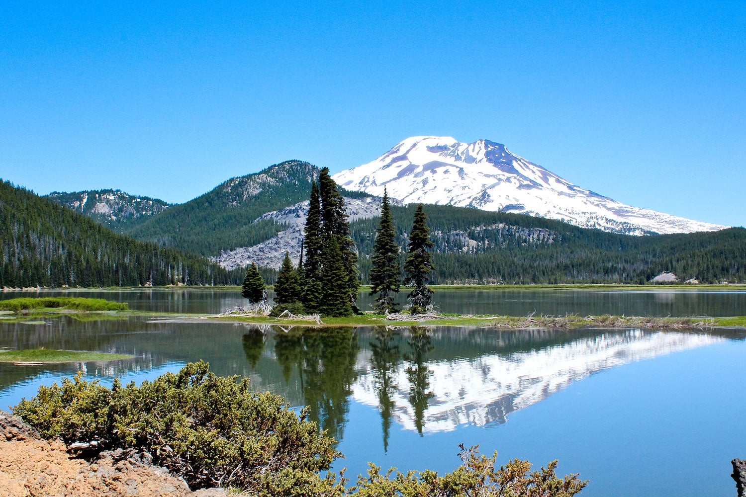 Snow covered peak rising over a lake with mountain reflection on water