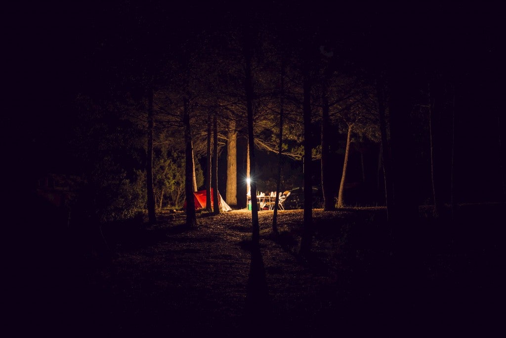 Lantern lighting up a campsite in the woods at night.