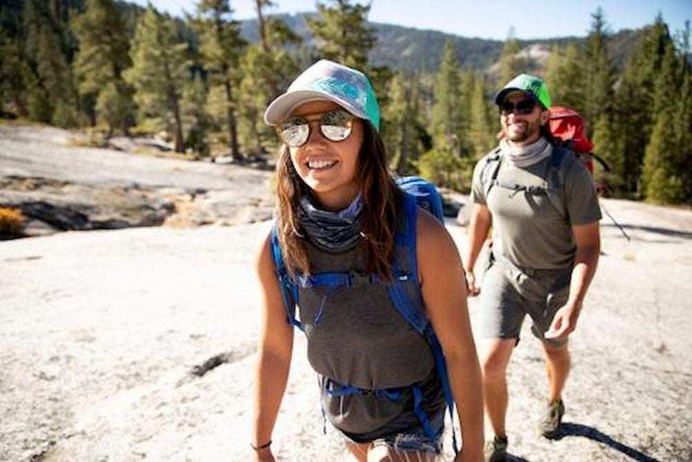 Hiking couple with backpacks, hats, and sunglasses.