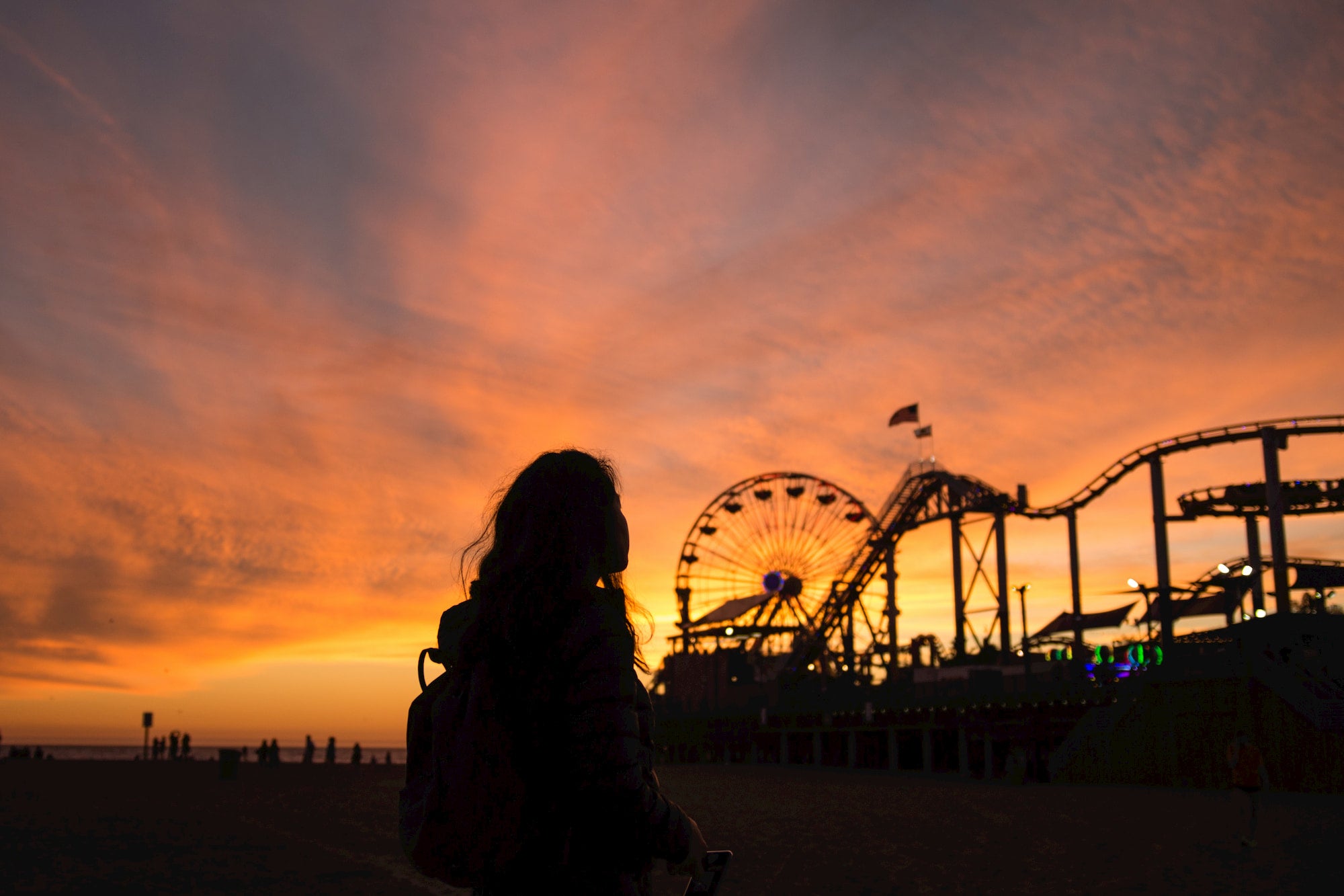 Silhouette of a woman at sunset on a pier with a ferris wheel.