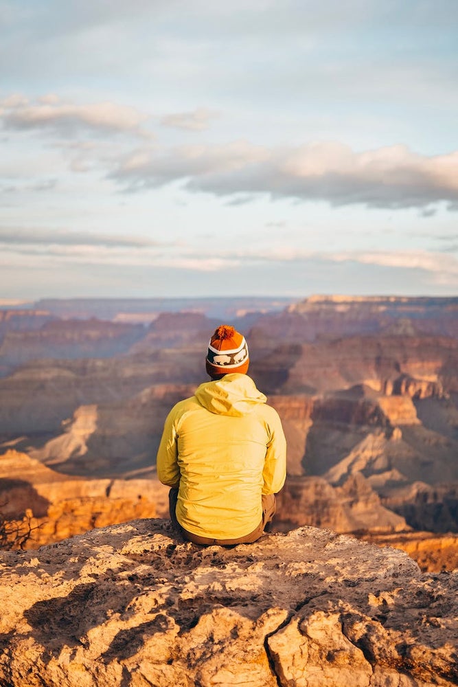 Person is puffer jacket and beanie sitting and watching the sunset over the Grand Canyon.
