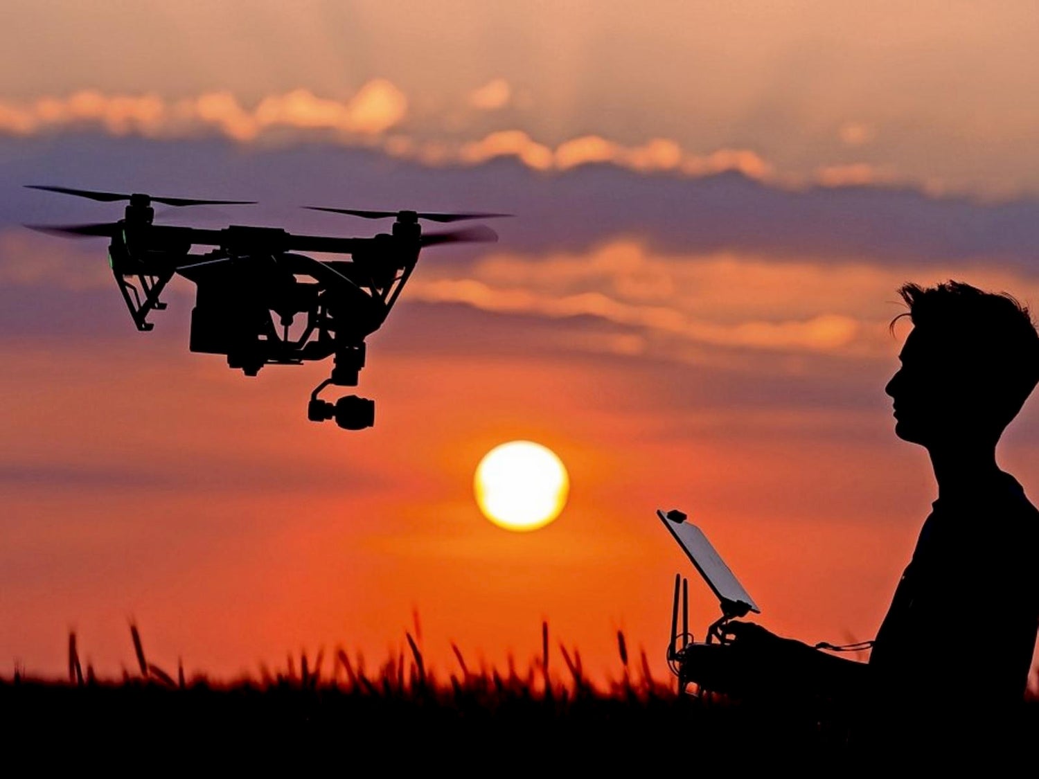 silhouette of person flying drone in sunset