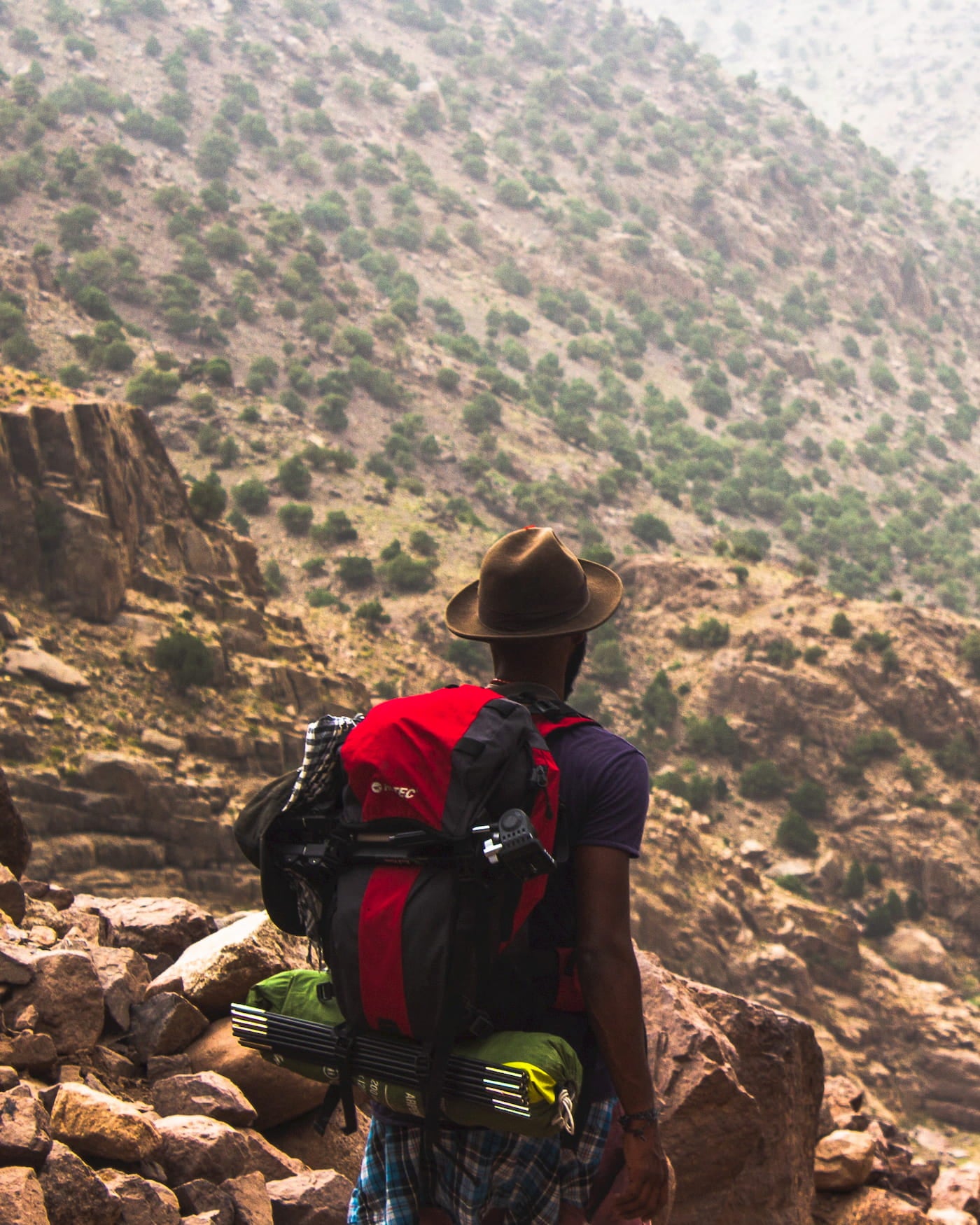 Hiker carrying backpack with camping gear in a desert landscape.