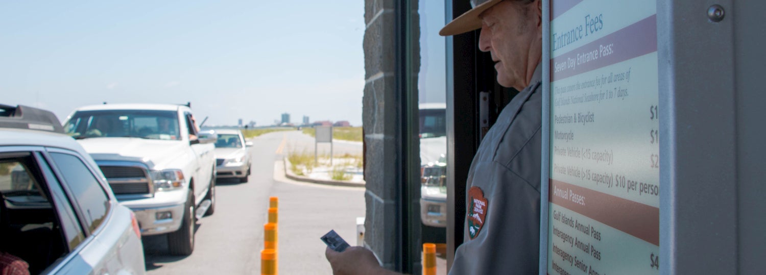 ranger inspecting national parks pass with line of cars in the background