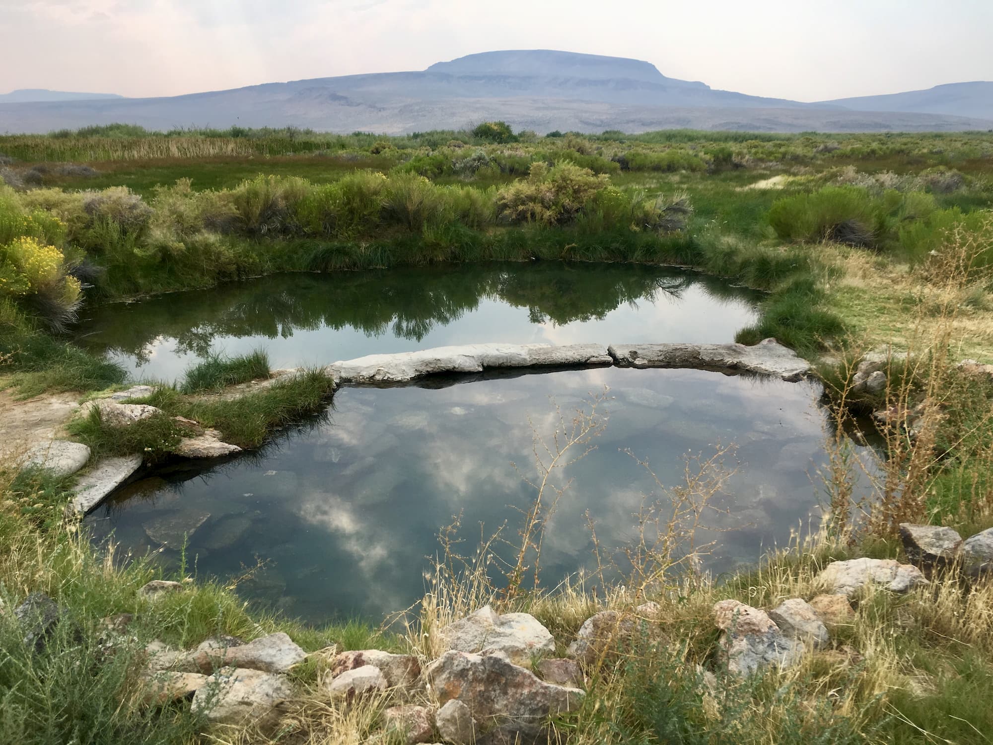 Hot spring surrounded by rocks and grass with rolling hills in the background.