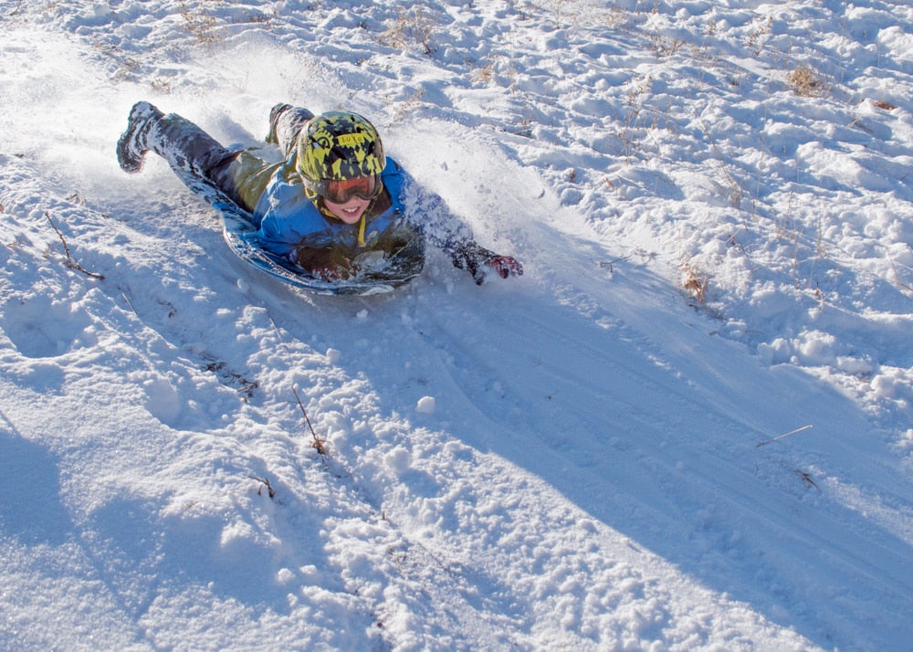 Young boy sledding down a snow covered hill.