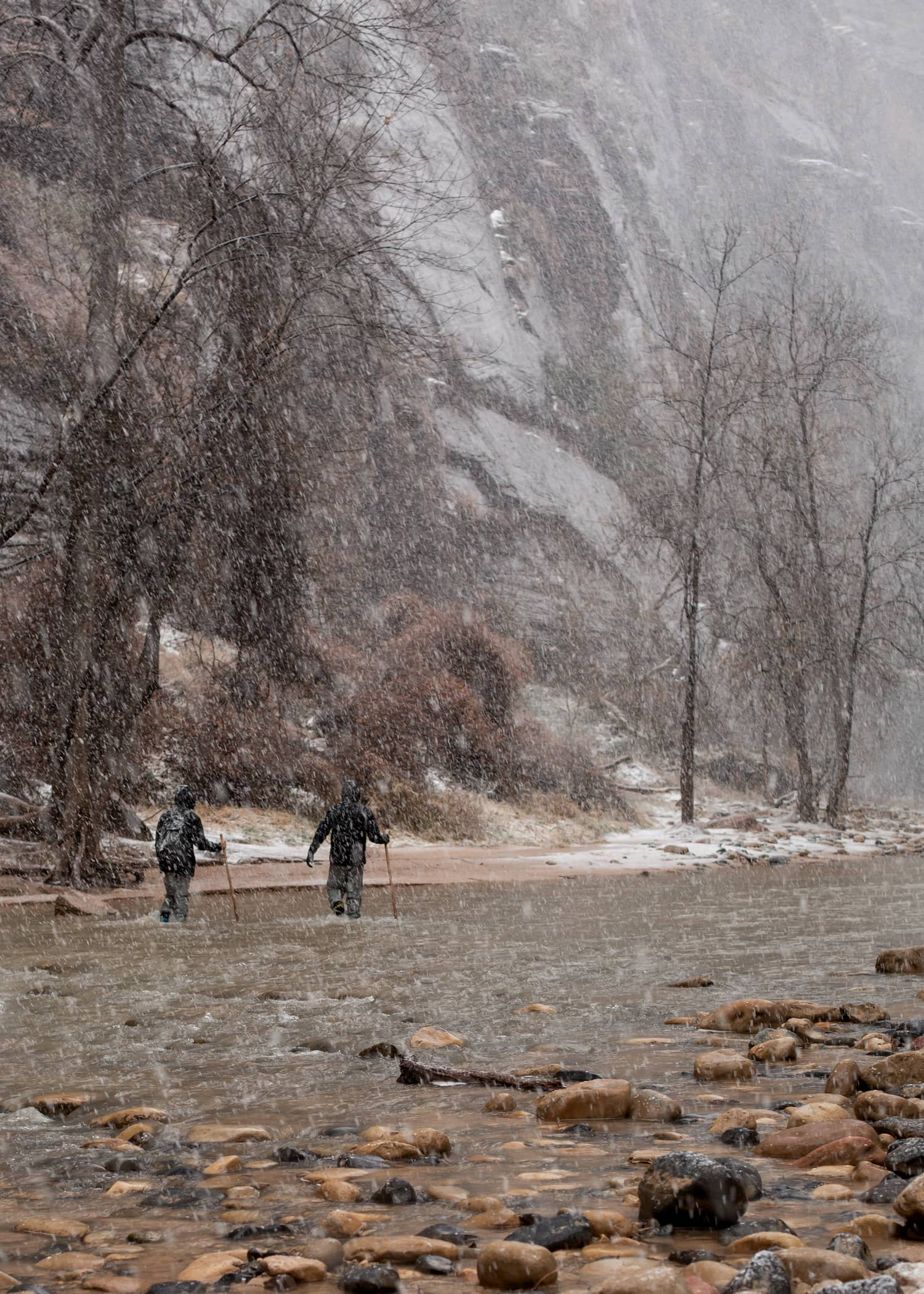 Two men make their way upstream in the Narrows in Zion national park on a cold snowy winter day.