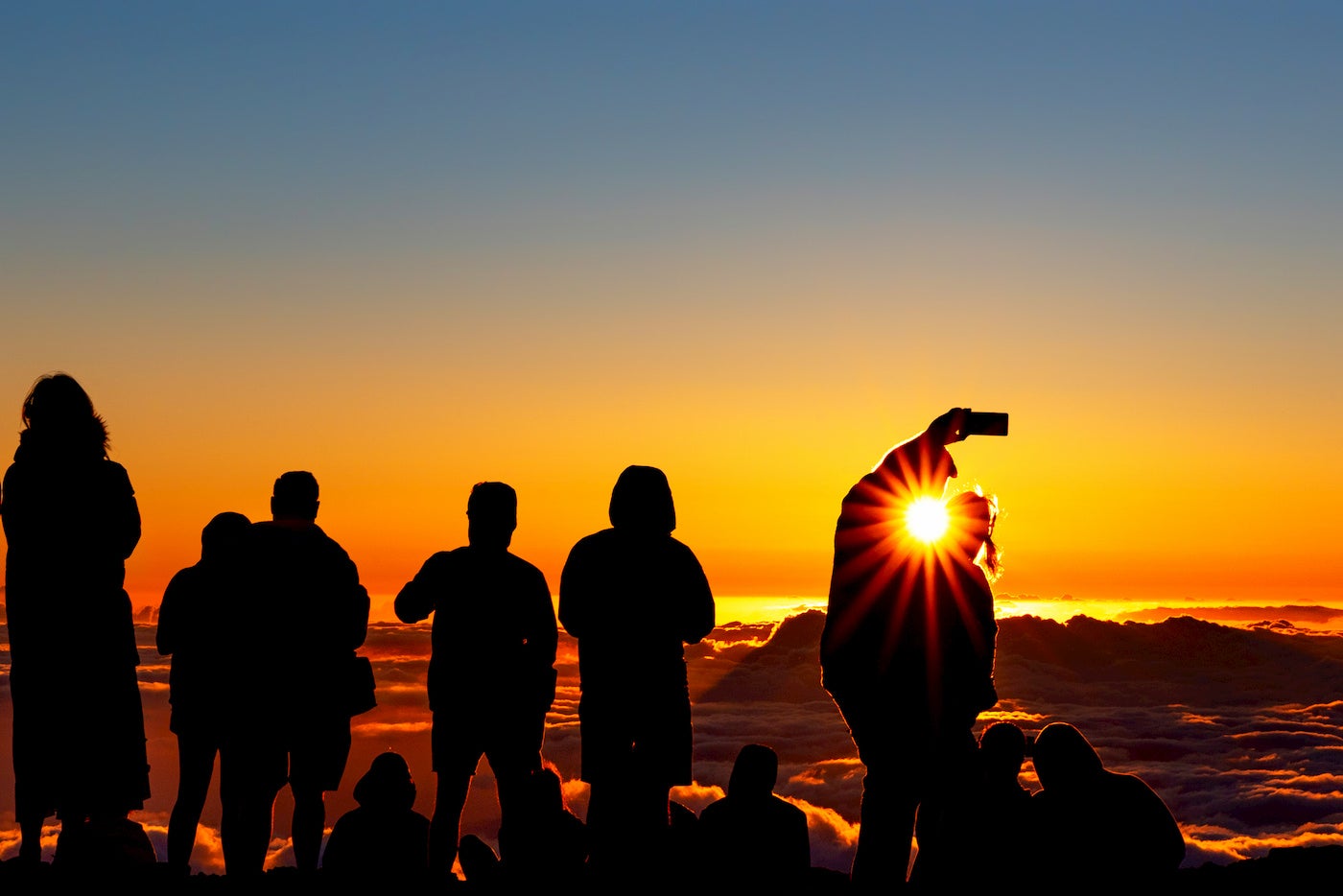 Group of people watching the sunset above the clouds on mountain.