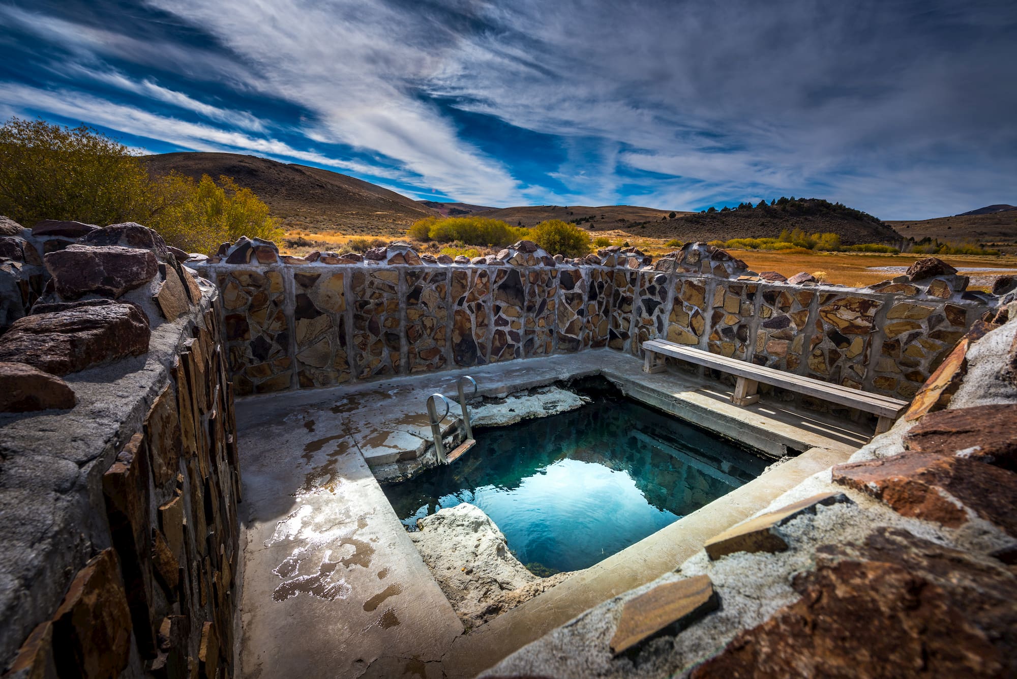 Hot spring surrounded by brick wall and pool with stairs in the mountains.