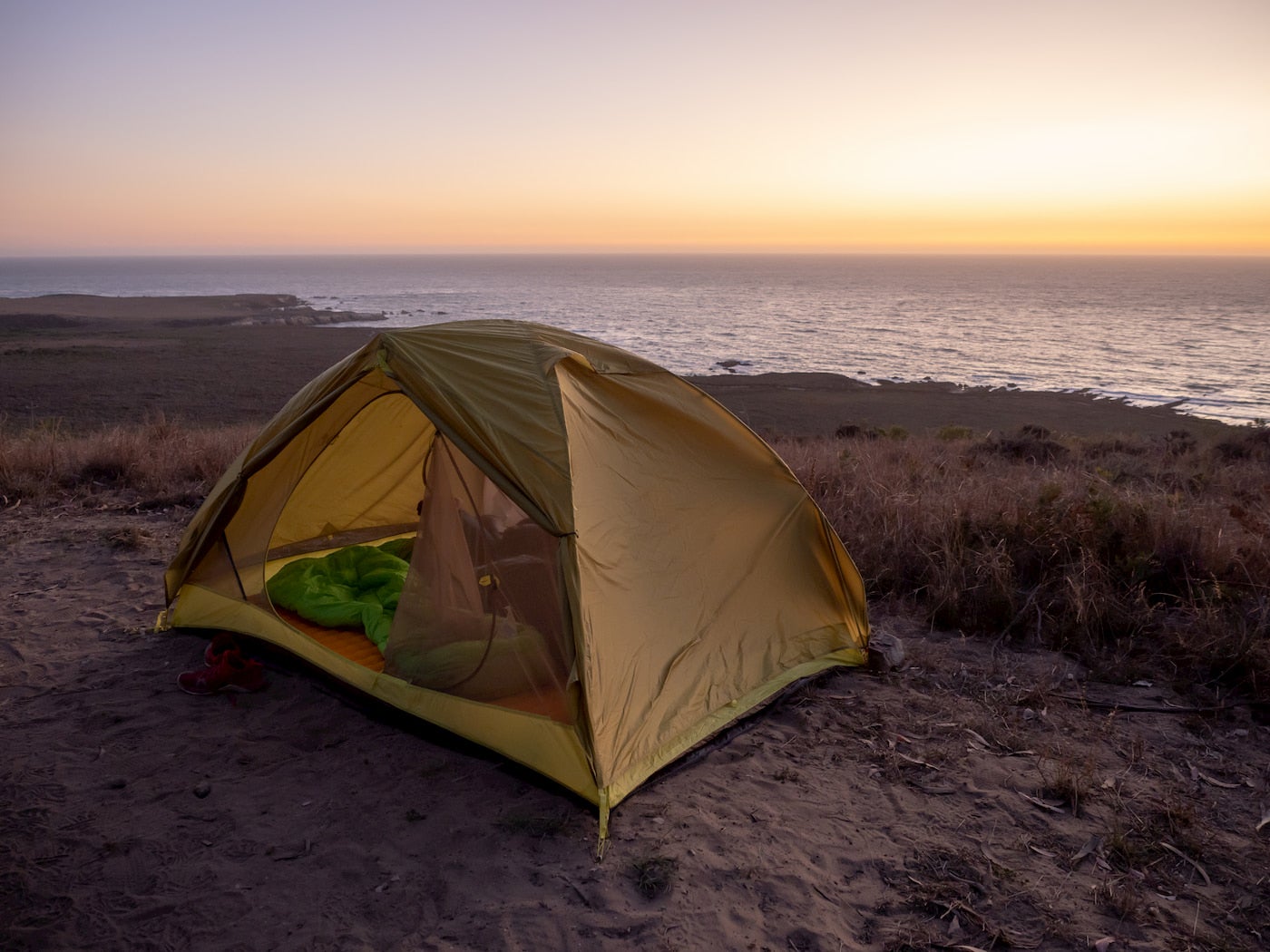 Tent set up in the dunes beside the pacific ocean at sunset.