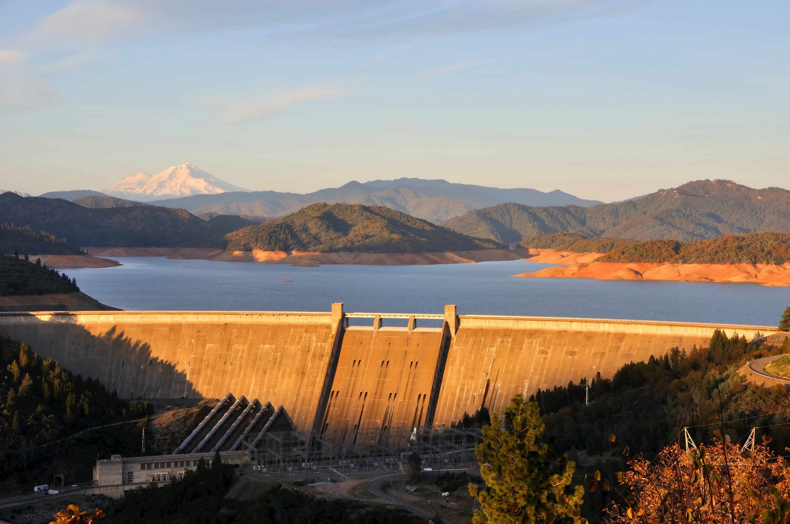 Golden sunlight over the Shasta Dam with MT. Shasta and green hills in the background.