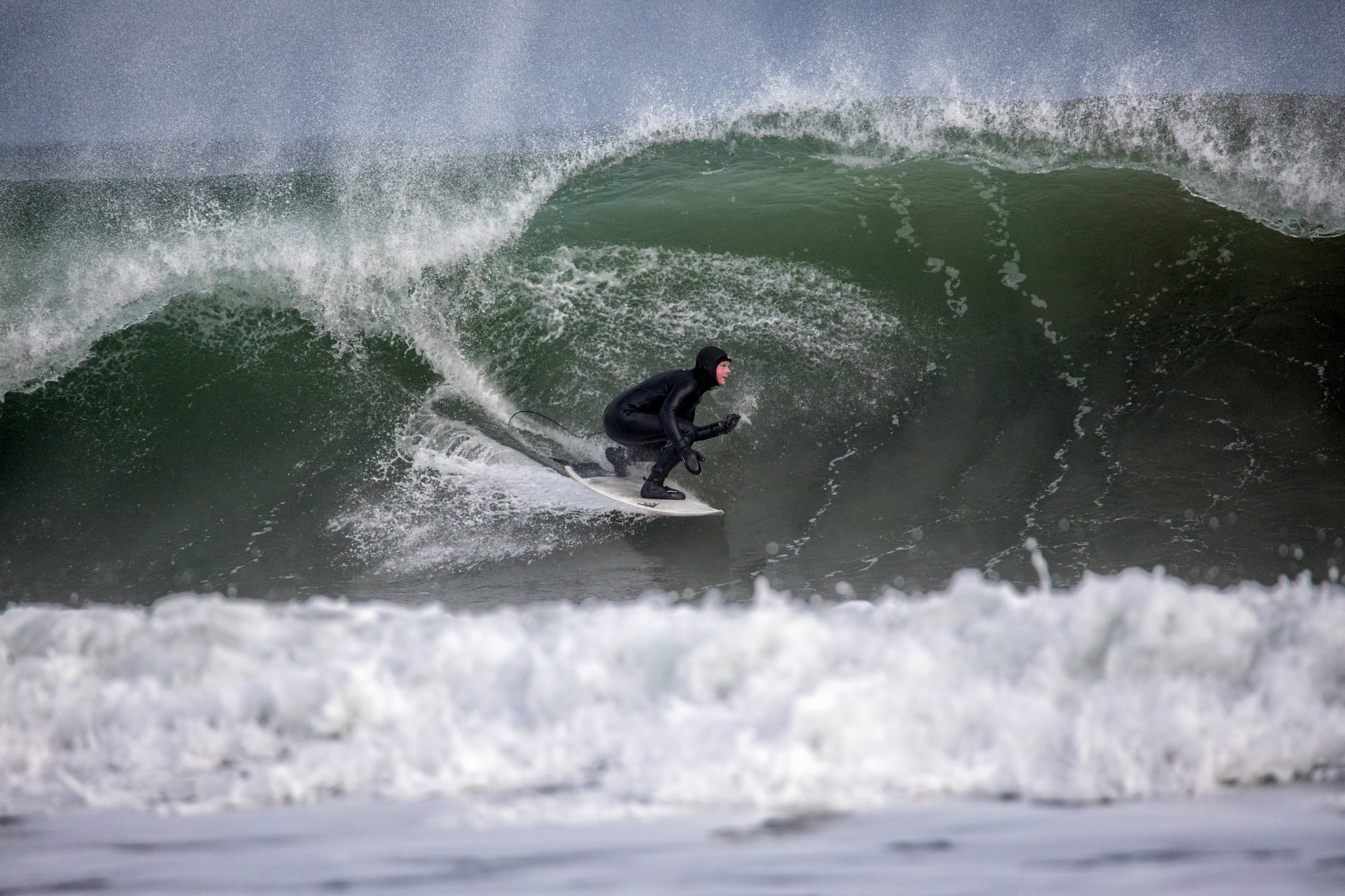 Man crouching on surfboard as he drops into large barreling wave.
