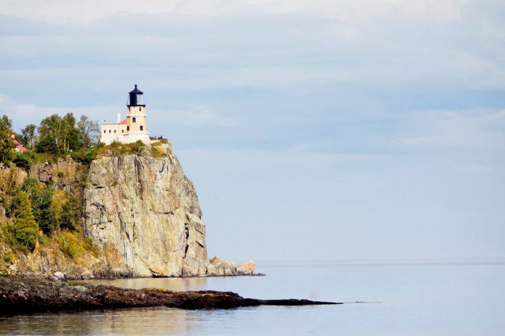 White lighthouse on edge of cliff facing the ocean.