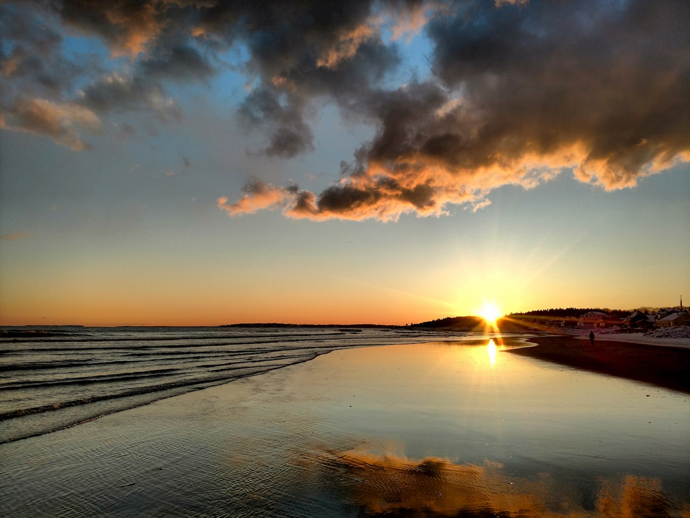 Sunset over a long stretch of beach at low tide.