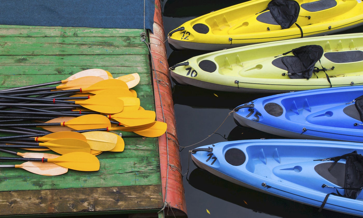 Kayaks tied up against a dock with a pile of paddles on it.